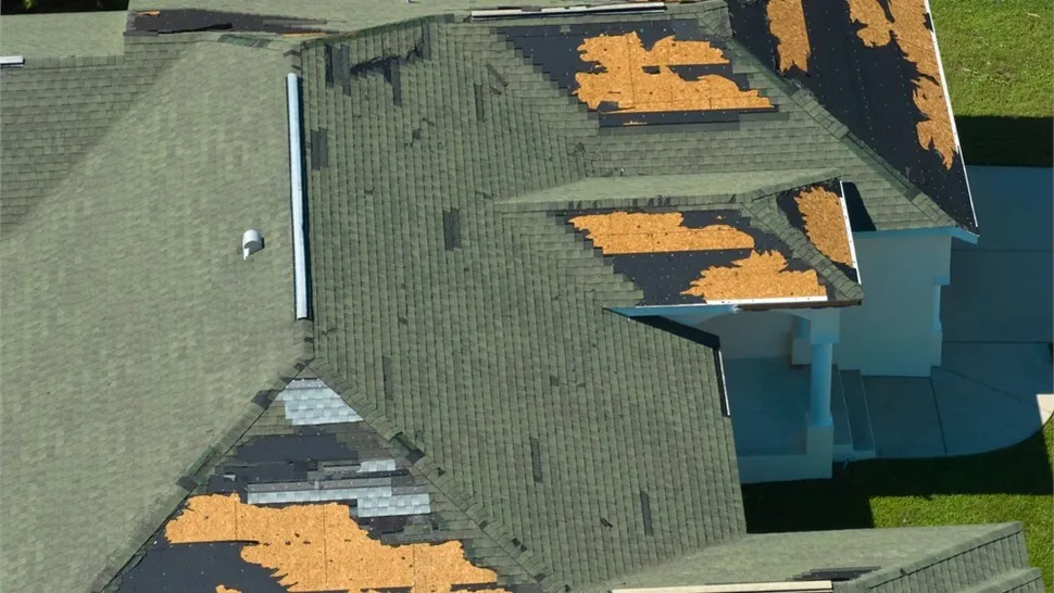 Aerial view of a roof with shingles torn away, exposing the underlayment