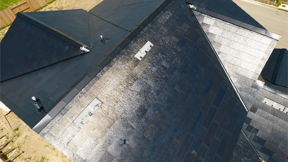 Aerial view of a solar shingle roof section beside asphalt shingle slopes