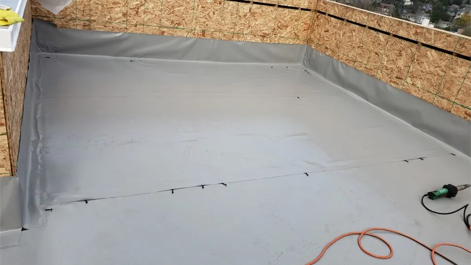 Worker fitting a seam strip on a white single-ply commercial membrane roof
